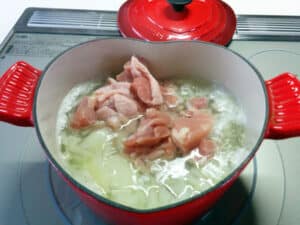 ルクルーゼの赤い鍋にチキンを入れる